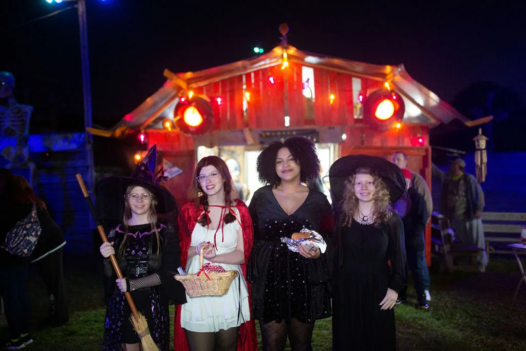 Four guests in costume outside the ticket barn: a witch with a broom, Little Red Riding Hood, a woman in a starry black dress and a witch in a wide hat